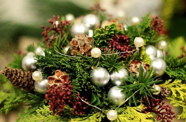 Celebrate Yule and Solstice decoration featuring greenery arrangement featuring evergreens, pine cones and silver spheres.