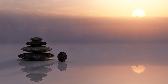 Using Reiki to create balance for body, mind and spirit is depicted through a pile of rocks balanced on top of each other with a sunset behind it.