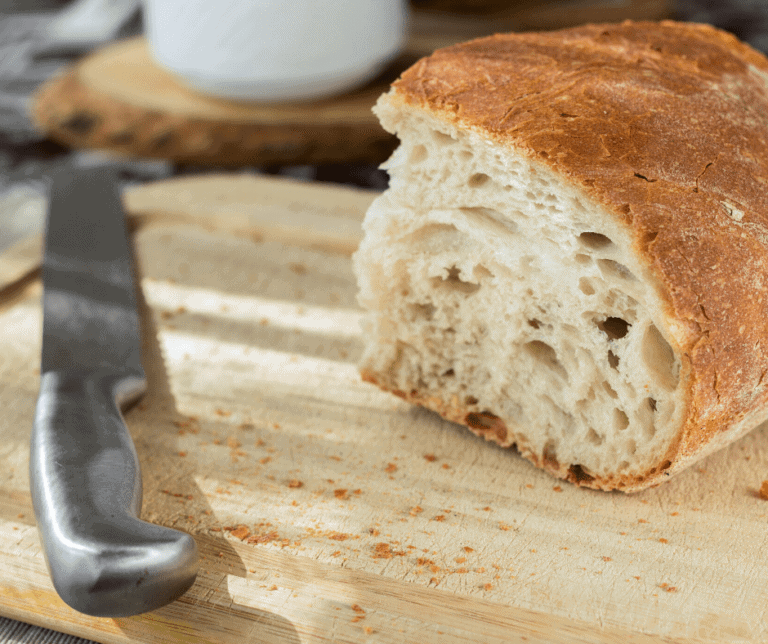 Loaf of fresh baked bread on a bread board with a knife alongside.