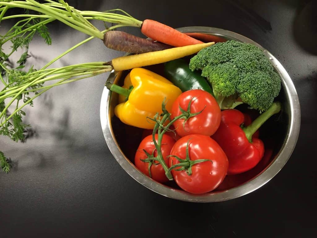 Eat a cleaner diet to reduce chemicals in your food. Bowl of fresh produce including carrots, peppers, broccoli and tomatoes.