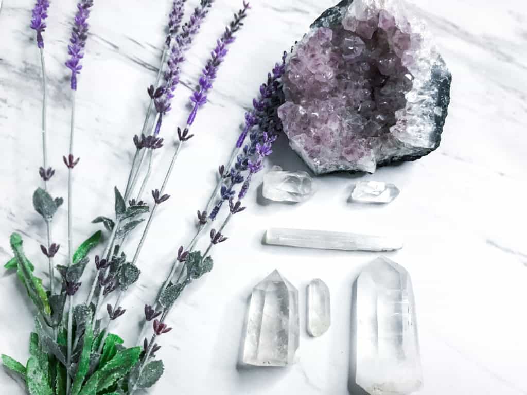 3 of the best crystals for meditation, featuring an amethyst geode, clear quartz, lavender flowers