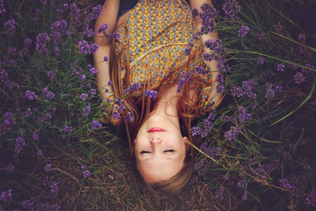 Girl laying in a lavender field, eyes closed, inhaling the aroma.