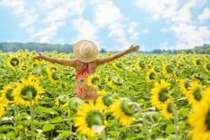 3 Ways to Get Happy With Mindfulness - woman celebrating in a field of sunflowers
