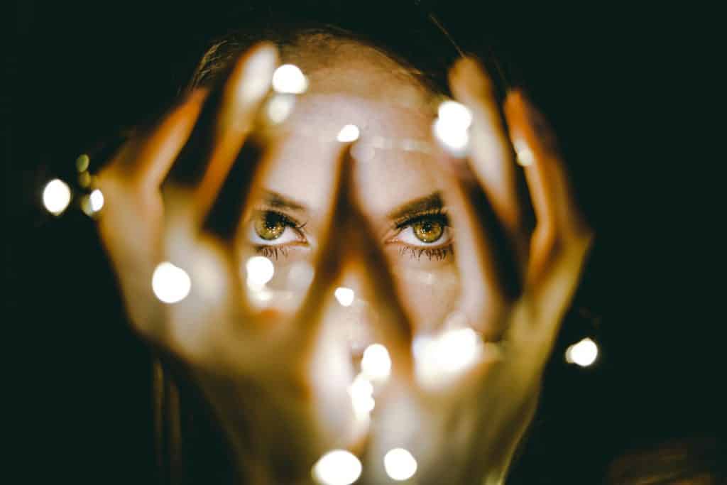 woman looking through her hands, draped in fairy lights. Look for the magic of Mercury Retrograde.