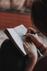 girl writing in a journal, all you see is her hands and hair as she's journaling 