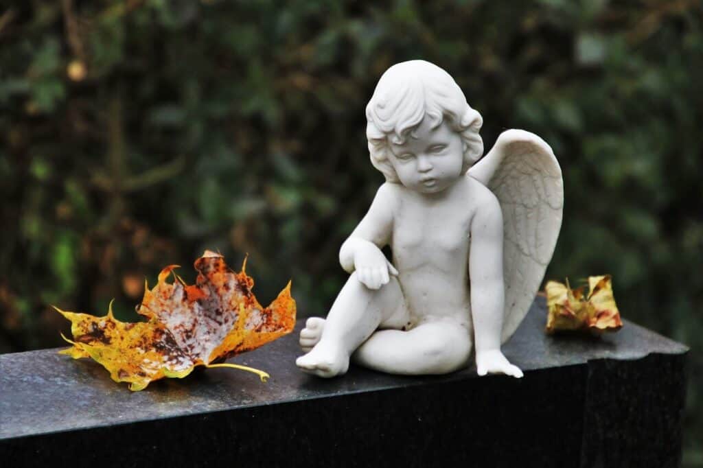 Cherub angel perched on top of a gravestone wtih autumn leaves around it. Losing mom blog post.
