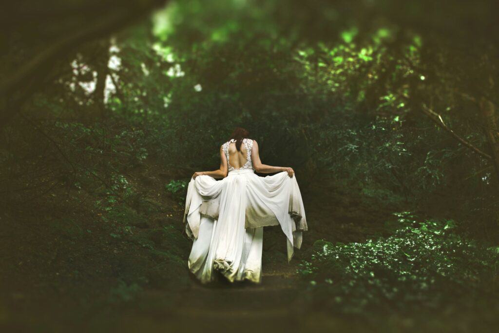 What is a green witch? Showing a woman walking away from the camera, wearing a long white dress. Going into a forest, depicting the green witch.