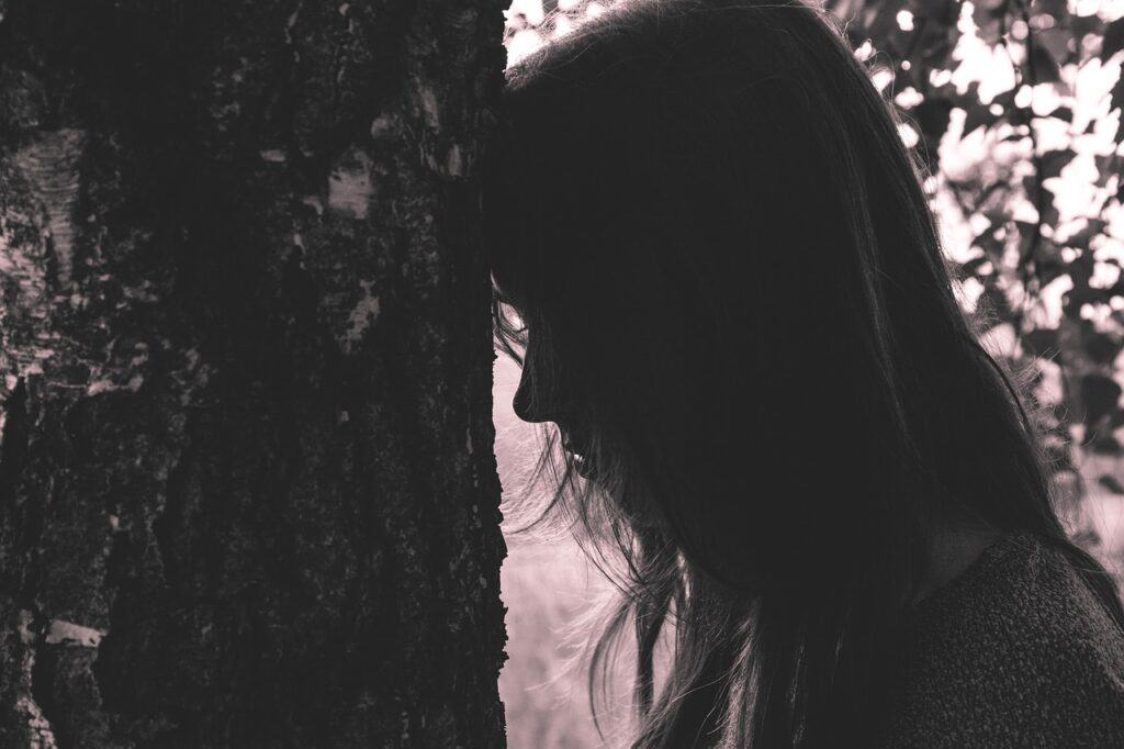 Girl with her forehead pressed against a tree in black and white photo to depict doing shadow work in the summer months .