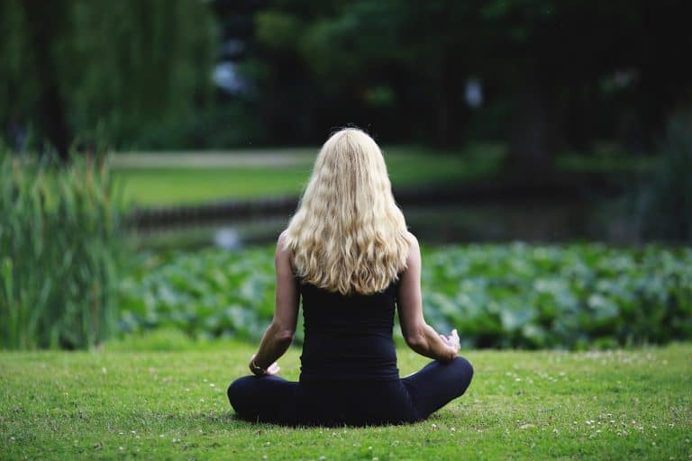 woman sitting near a pond with her back to us doing meditation