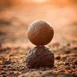 two round stones balanced one on top of the other on a beach background with setting sun.