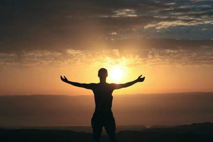 person with arms outstretched to sides looking into a sunset. image is only in shadow